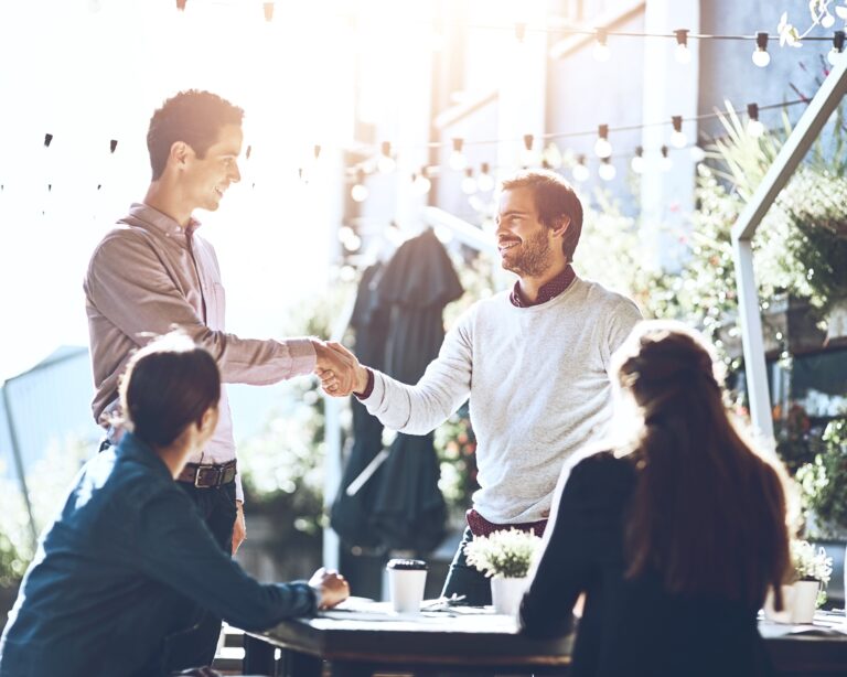 Business people, team and handshake in meeting at cafe for welcome, b2b networking or collaboration outdoor. Group, employees and shaking hands for intro, partnership deal or happy for agreement